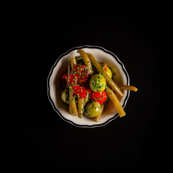 Appetizer bowl with green beans, red peppers, and green olives, garnished with chives.