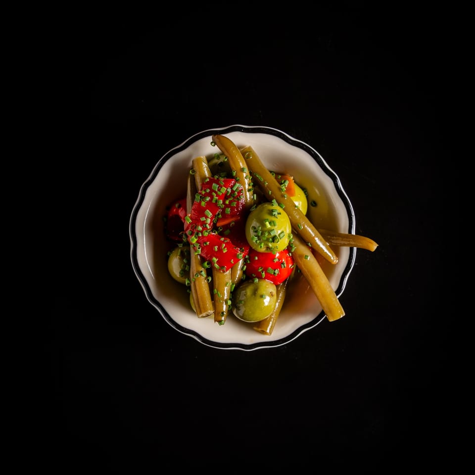 Appetizer bowl with green beans, red peppers, and green olives, garnished with chives.