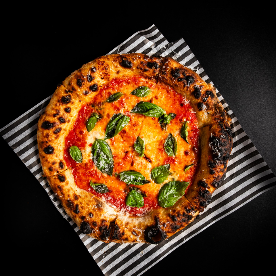 Neapolitan-style pizza with tomato sauce, melted cheese, fresh basil, grated cheese, and a charred crust on striped paper.