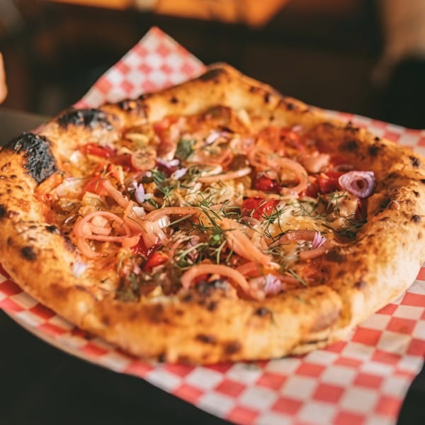 A close-up of a freshly baked pizza with red onions, peppers, and herbs on checkered paper.